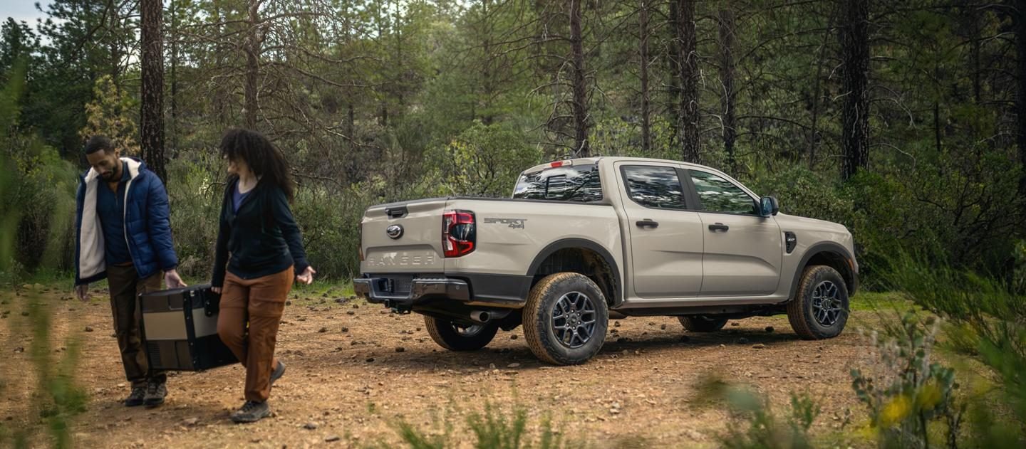 Ford Ranger color arena estacionada en un bosque con dos personas descargando equipo