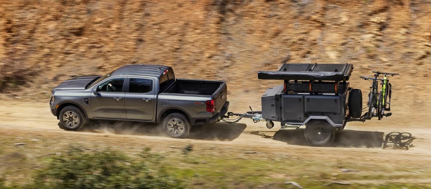 Ford Ranger gris remolcando un pequeño camper por un camino de tierra