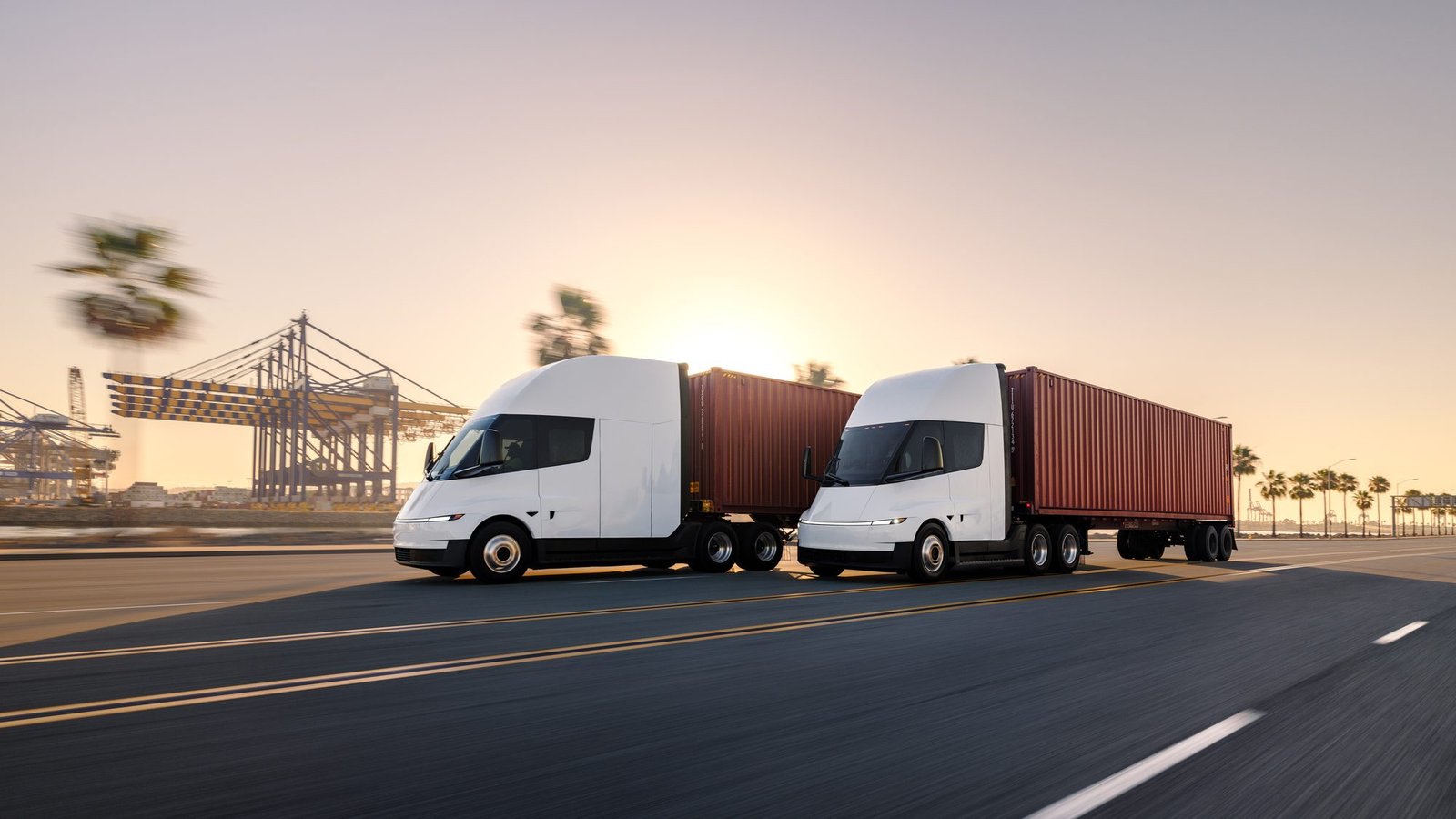 Dos Tesla Semi con contenedores rojos en una vía junto a grúas portuarias