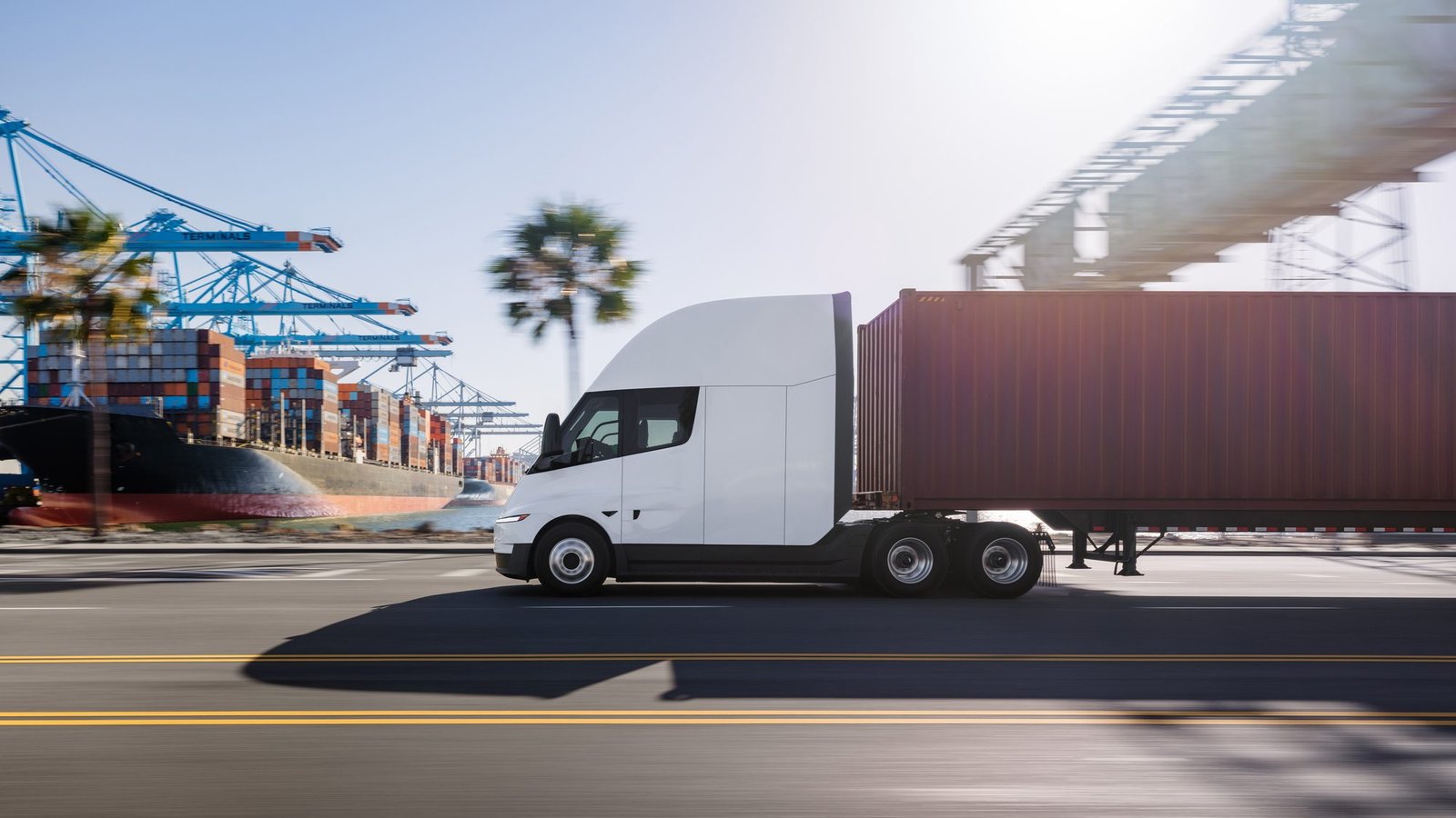 Tesla Semi con contenedor circulando junto a un puerto con palmeras