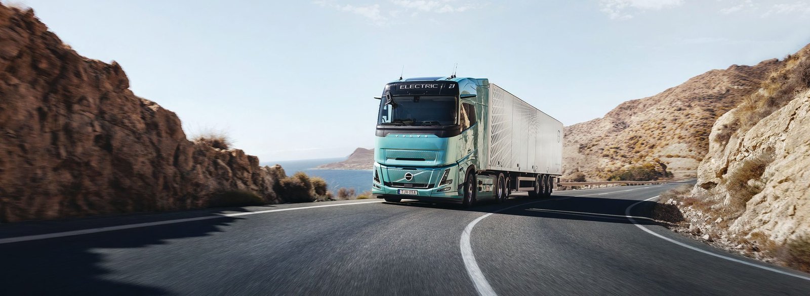 Volvo FH eléctrico con remolque en una carretera costera entre montañas