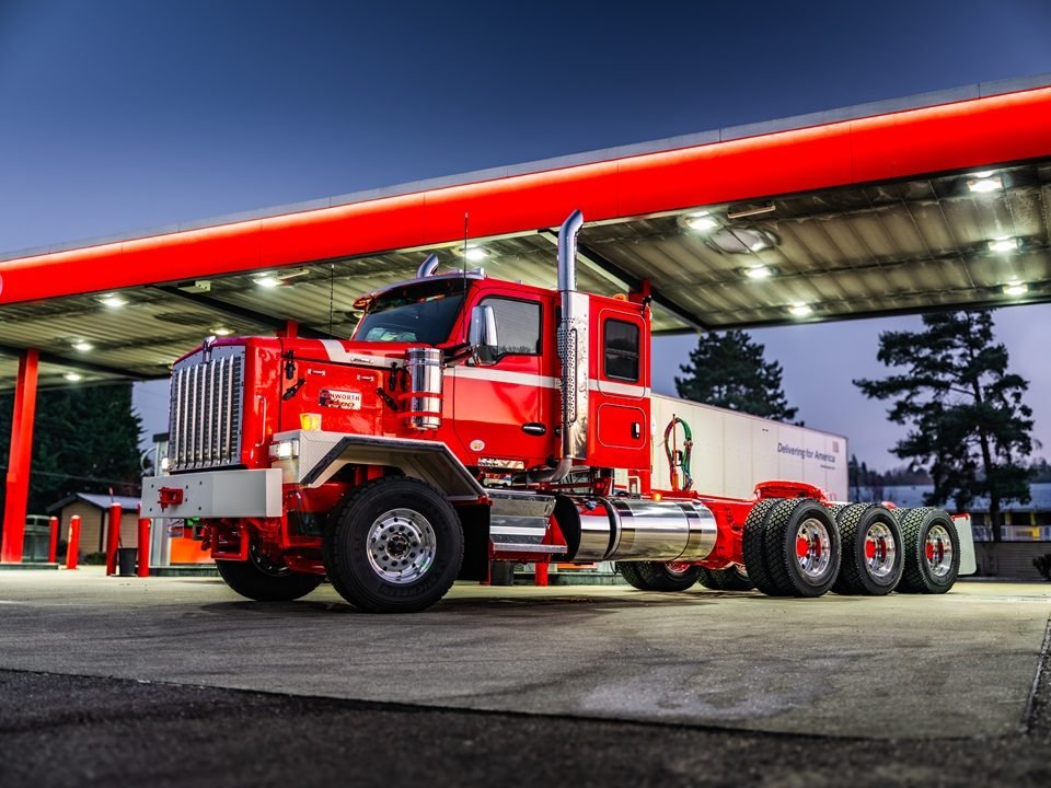 Kenworth C580 rojo bajo el techo iluminado de una gasolinera al anochecer