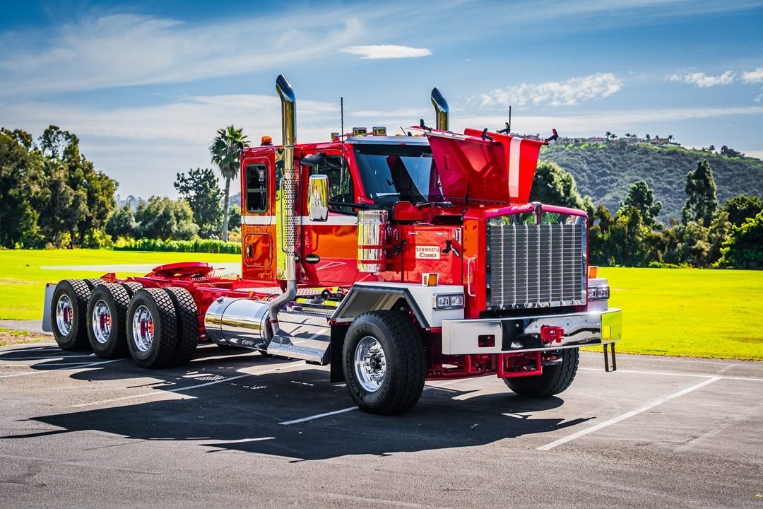 Kenworth C580 rojo estacionado en un lote junto a palmeras